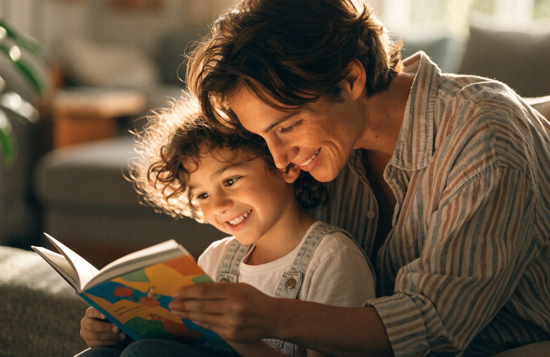 A parent and young child reading a picture book together and smiling in warm natural light